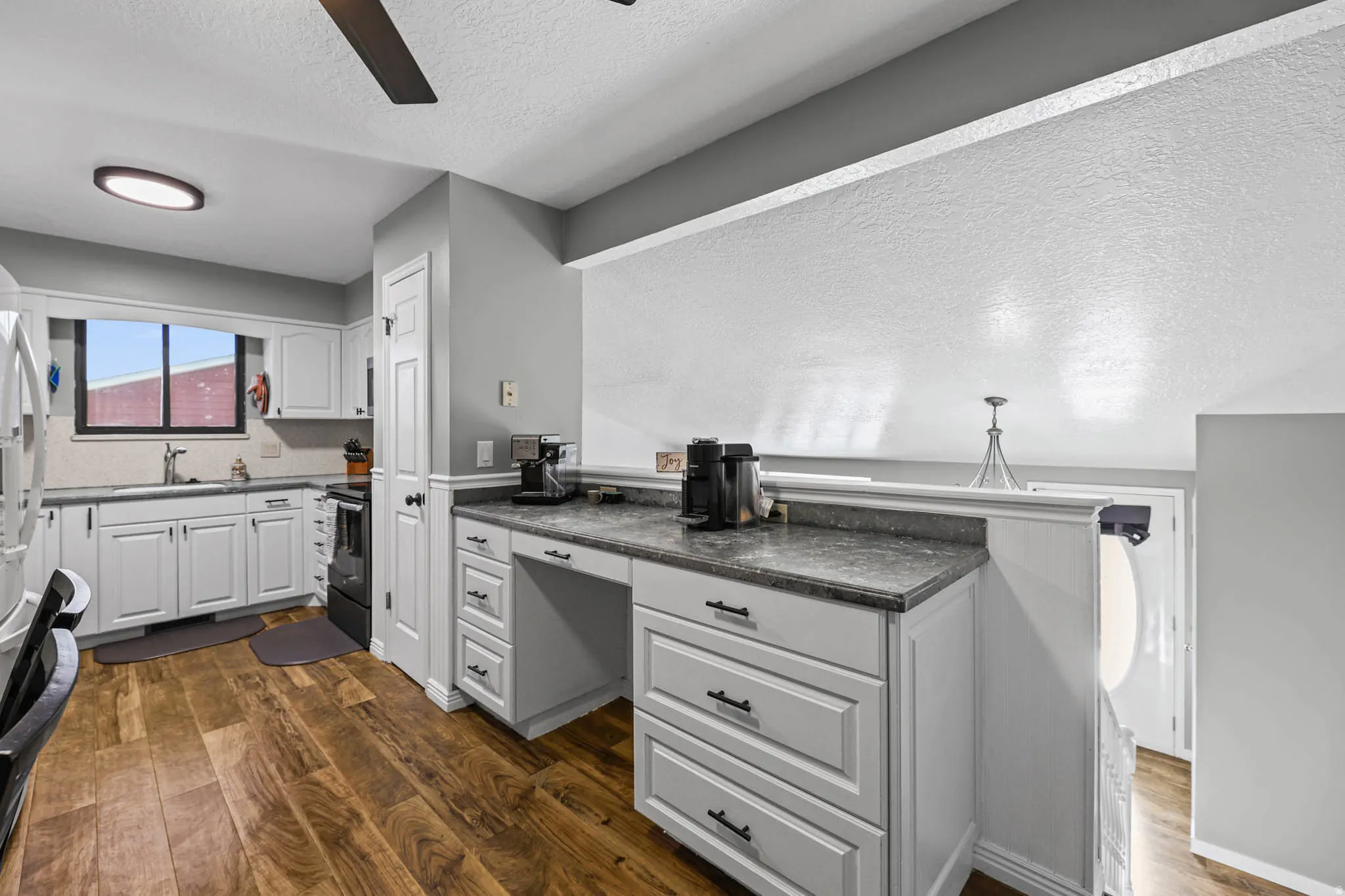 Kitchen featuring a textured ceiling, dark wood-style flooring, white cabinets, a ceiling fan, and dark countertops
