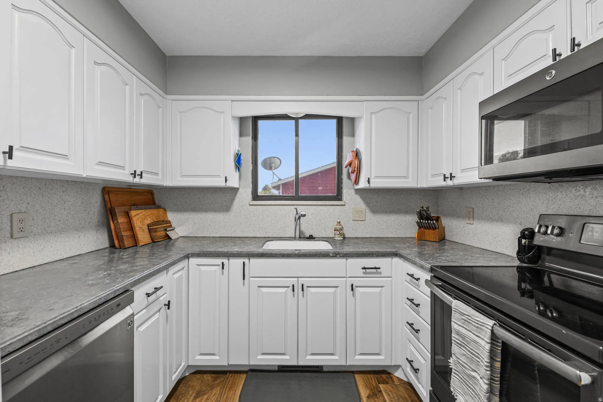 Kitchen featuring stainless steel appliances, white cabinets, dark countertops, and dark wood-type flooring