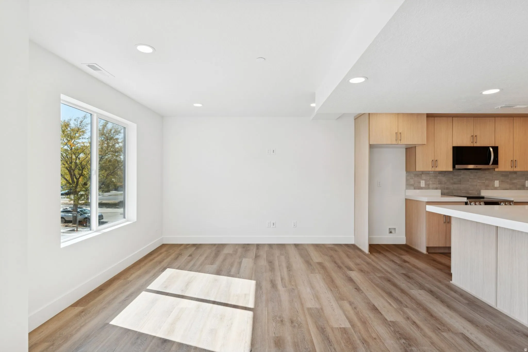 Kitchen featuring light countertops, light wood finished floors, modern cabinets, stainless steel microwave, and recessed lighting
