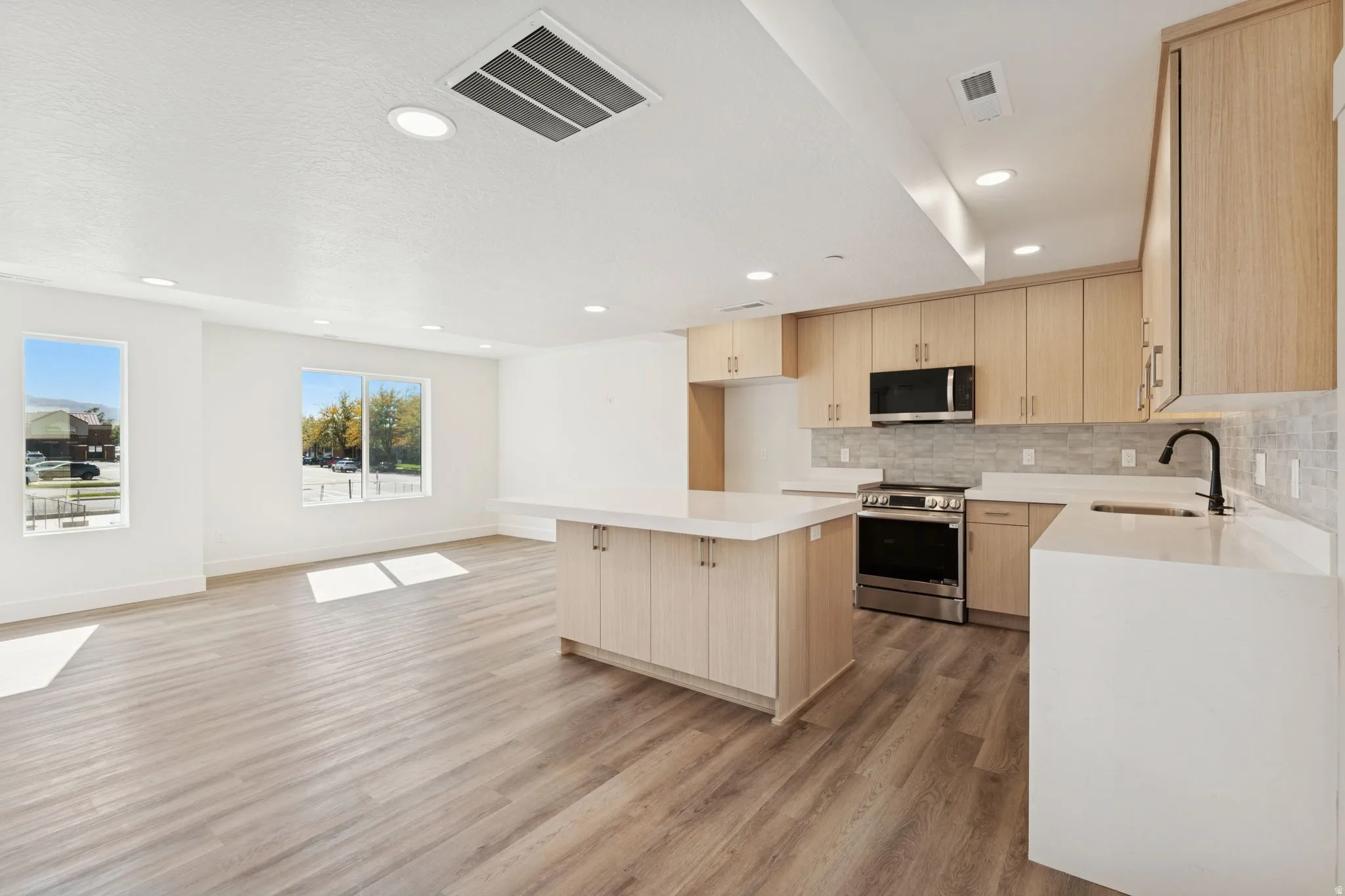 Kitchen featuring light wood finish cabinetry, stainless steel appliances, a kitchen island, open floor plan, and light wood-style flooring