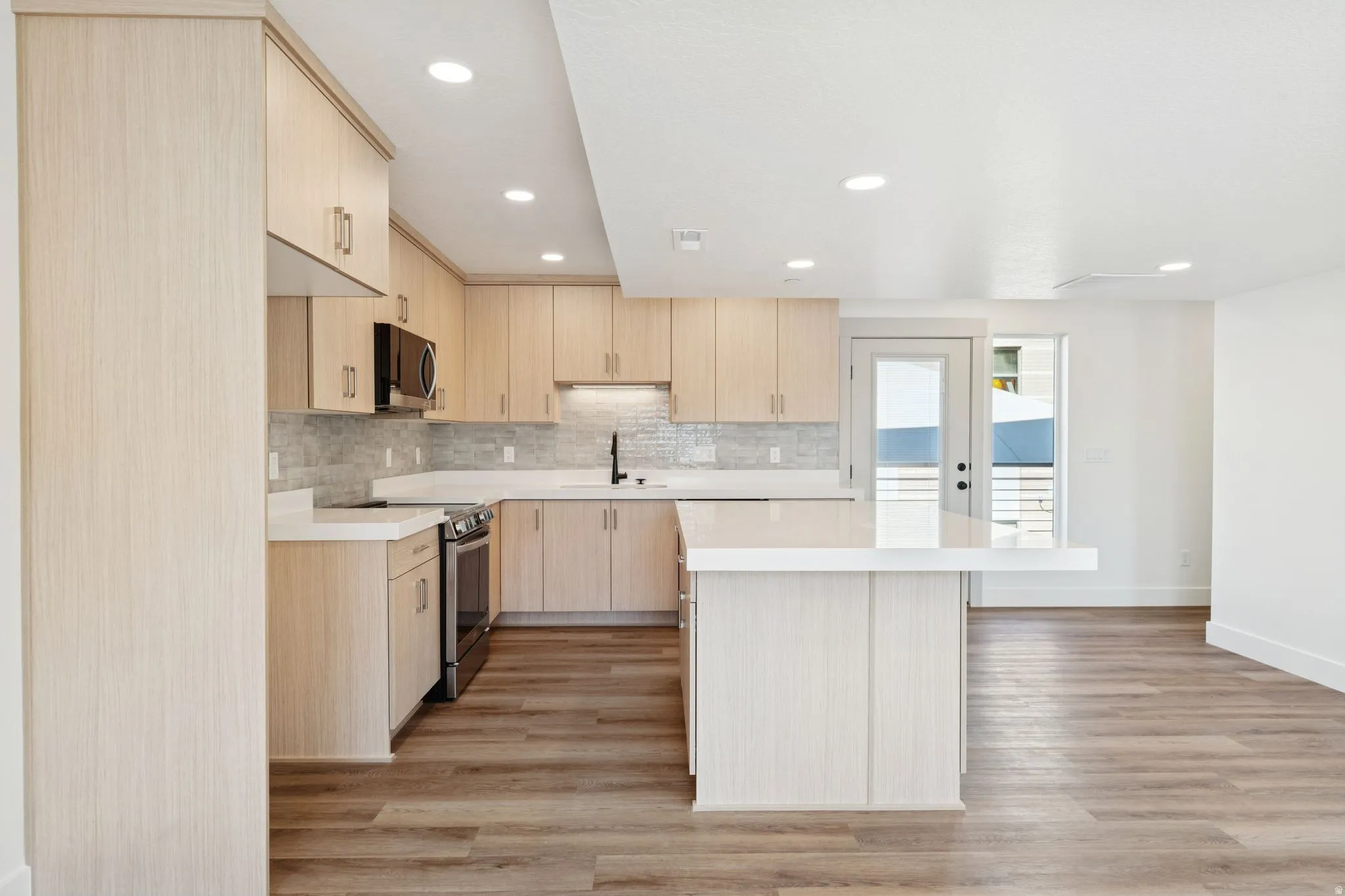 Kitchen featuring light wood finish cabinetry, a center island, stainless steel appliances, light wood-type flooring, and decorative backsplash