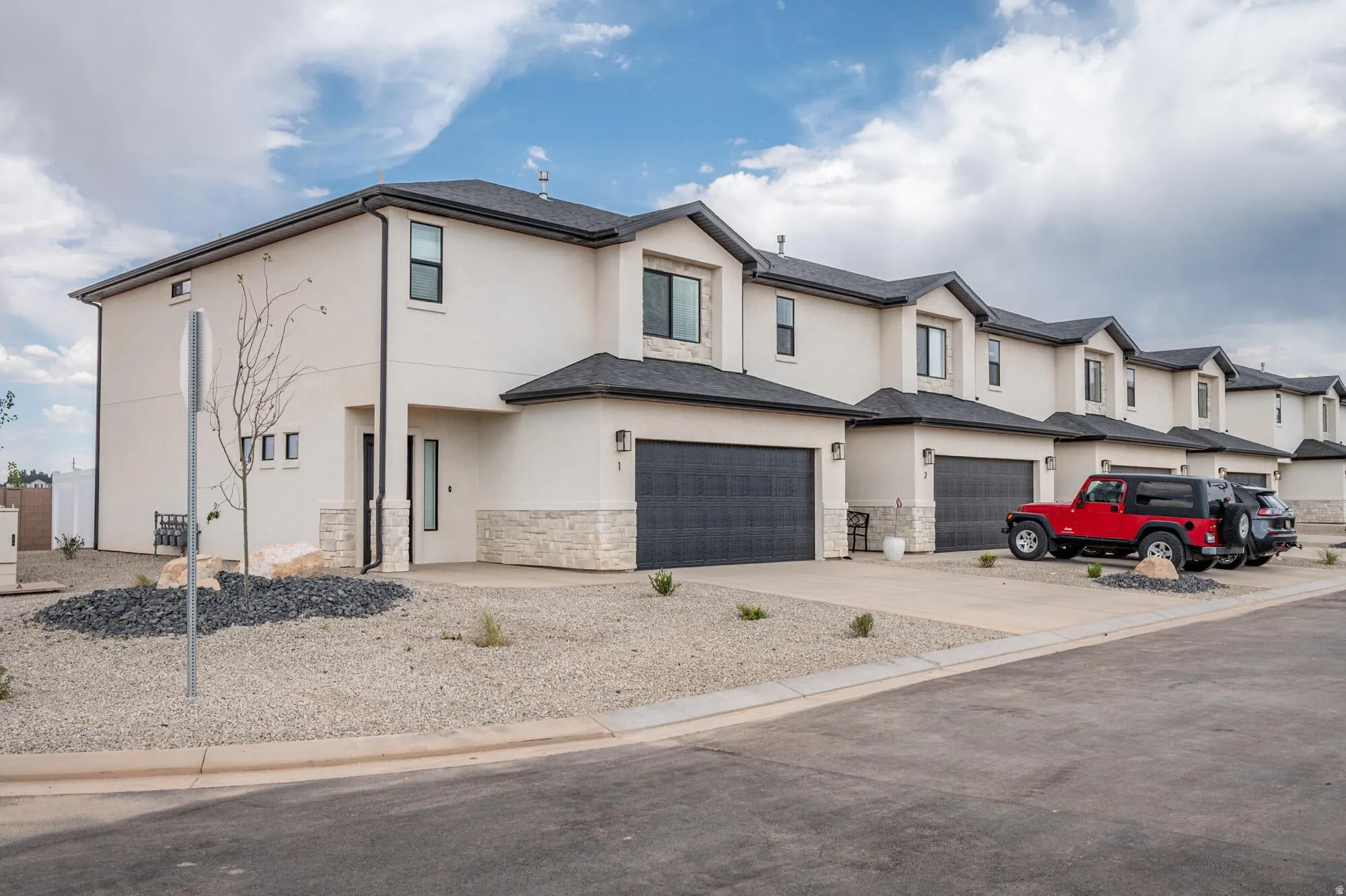 View of front facade with stucco siding, driveway, stone siding, a residential view, and an attached garage