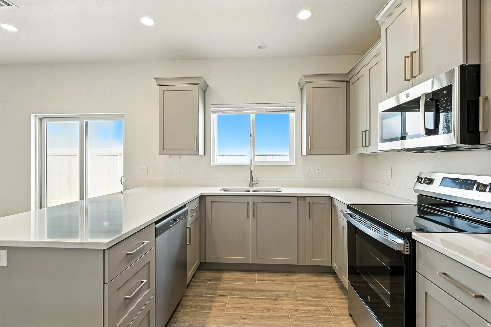 Kitchen with gray cabinets, stainless steel appliances, a peninsula, recessed lighting, and wood finish floors
