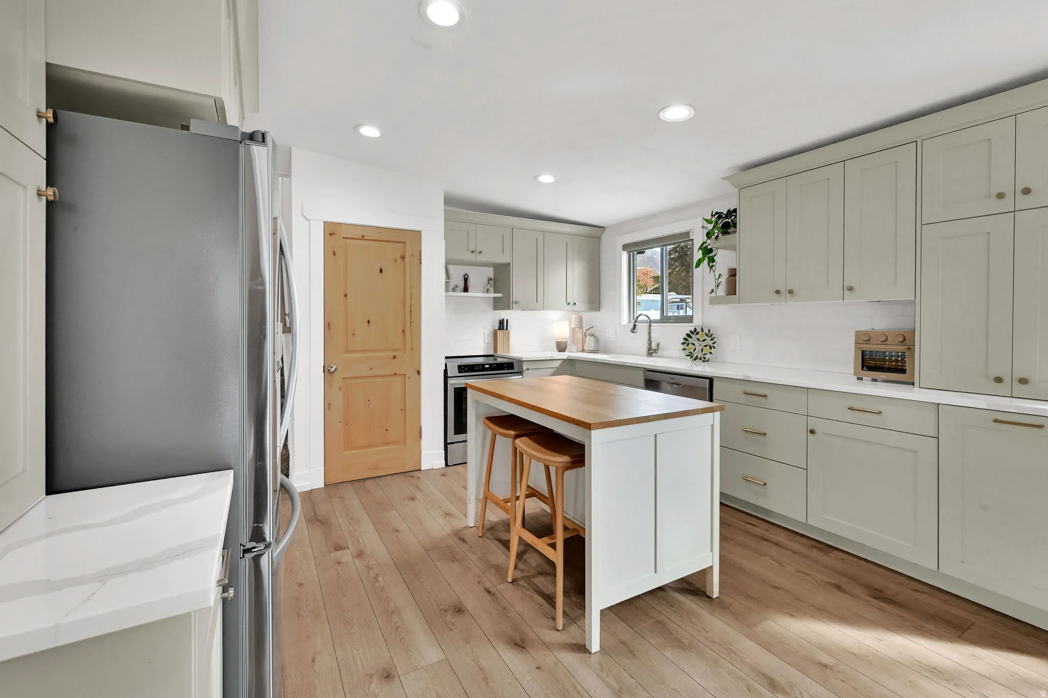 Kitchen featuring a breakfast bar, open shelves, appliances with stainless steel finishes, light wood-type flooring, and decorative backsplash