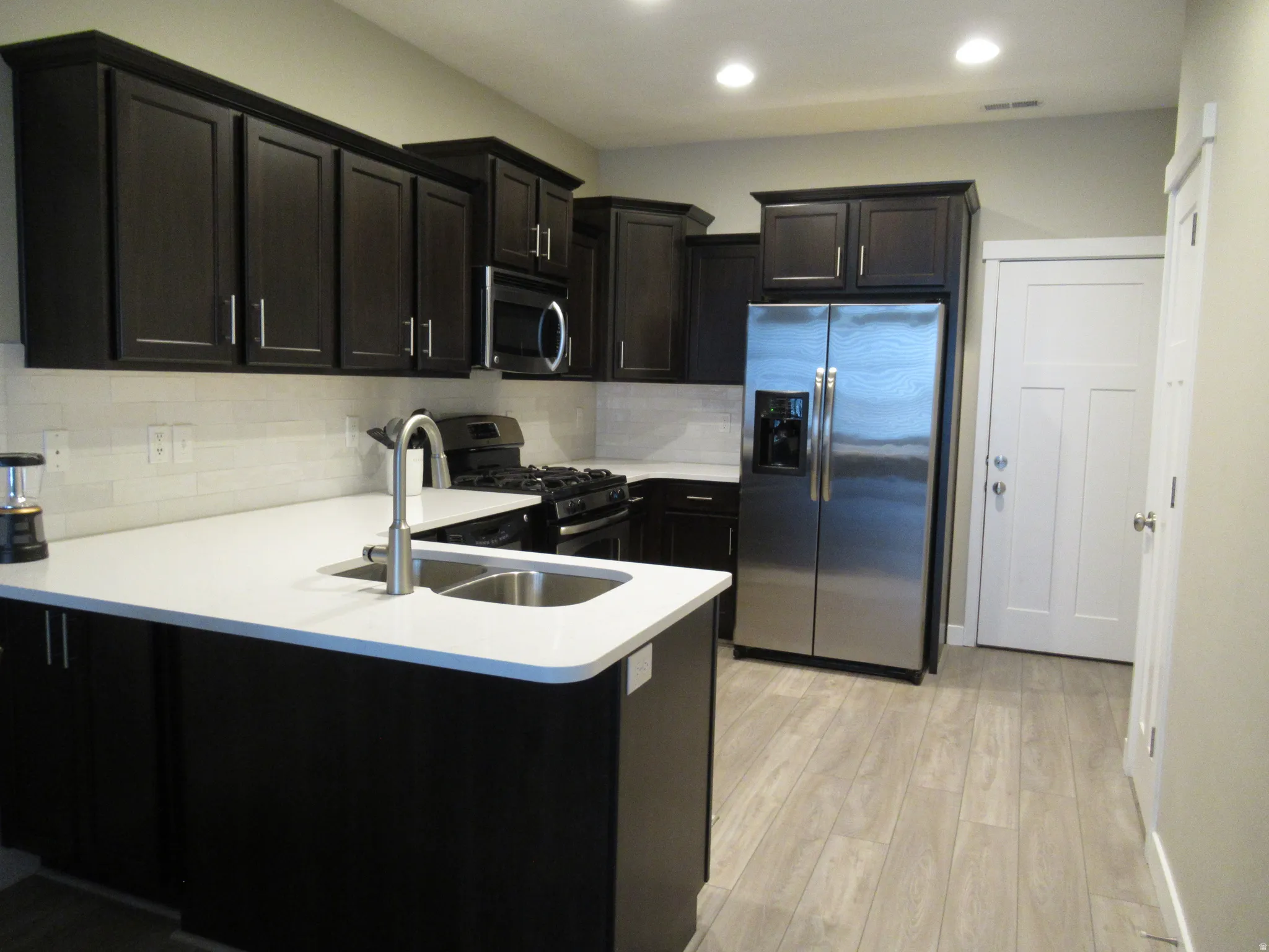 Kitchen with stainless steel appliances, light wood finished floors, a peninsula, dark cabinets, and recessed lighting