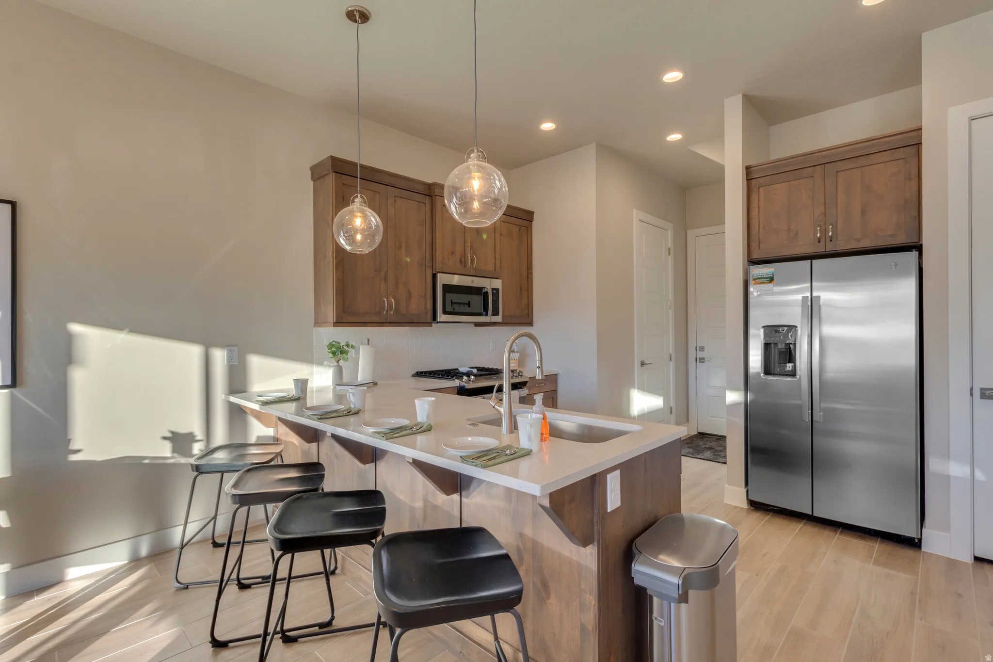Kitchen featuring stainless steel appliances, light wood-type flooring, a peninsula, a kitchen breakfast bar, and hanging light fixtures