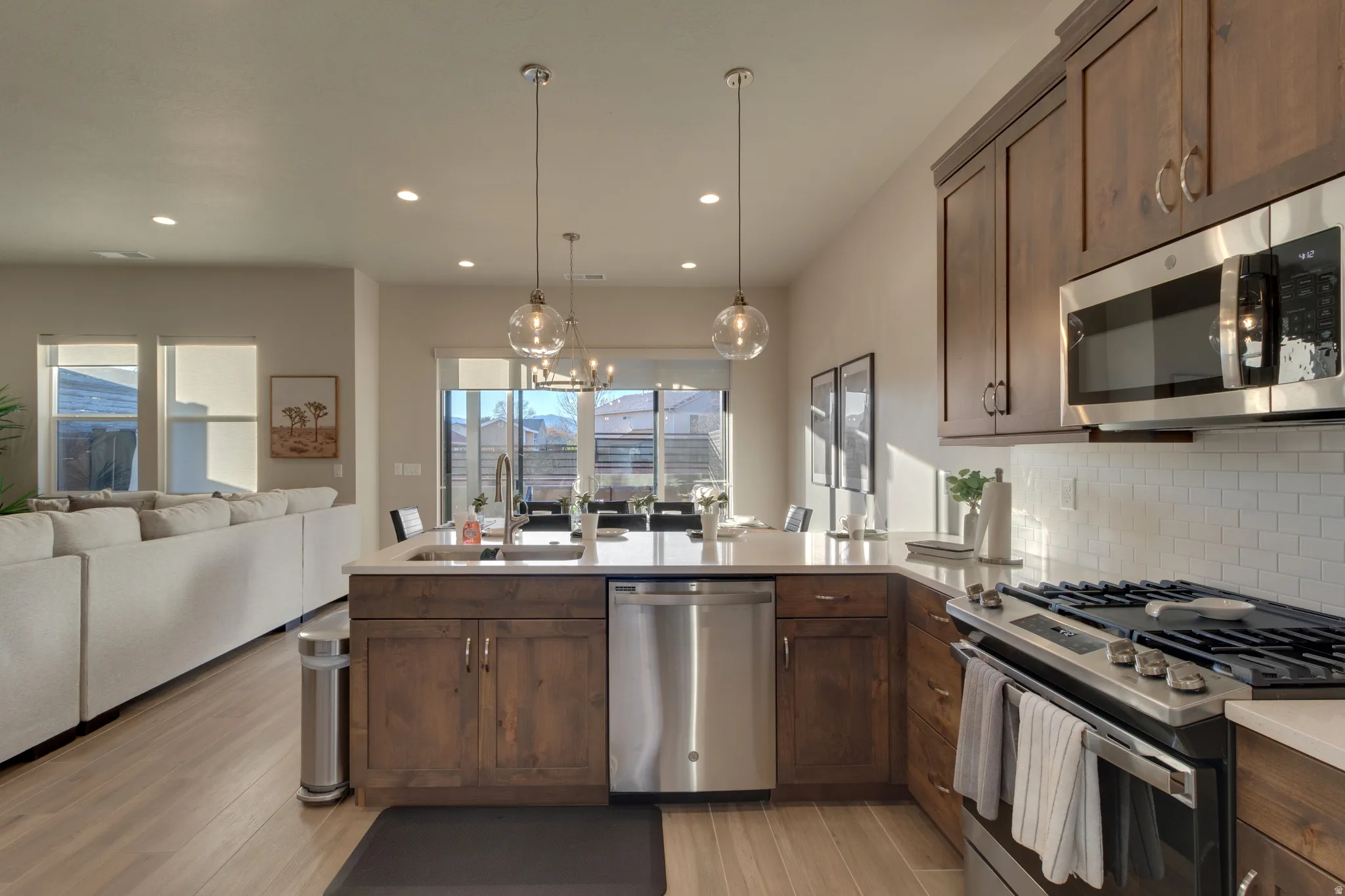 Kitchen featuring stainless steel appliances, a peninsula, open floor plan, hanging light fixtures, and light wood-type flooring
