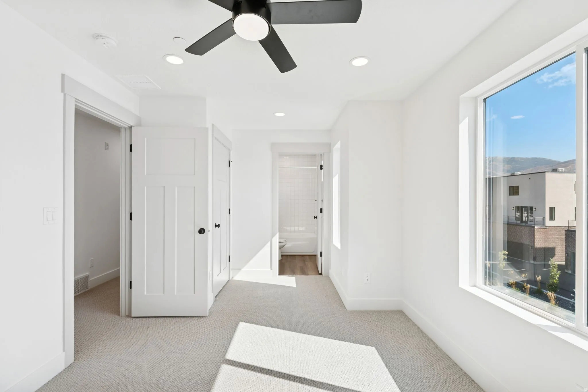 Unfurnished bedroom featuring connected bathroom, light colored carpet, a ceiling fan, and recessed lighting