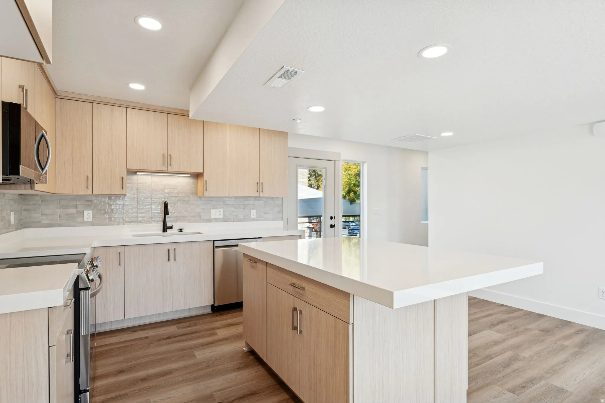 Kitchen with light wood finish cabinetry, a kitchen island, light wood-style floors, stainless steel appliances, and recessed lighting