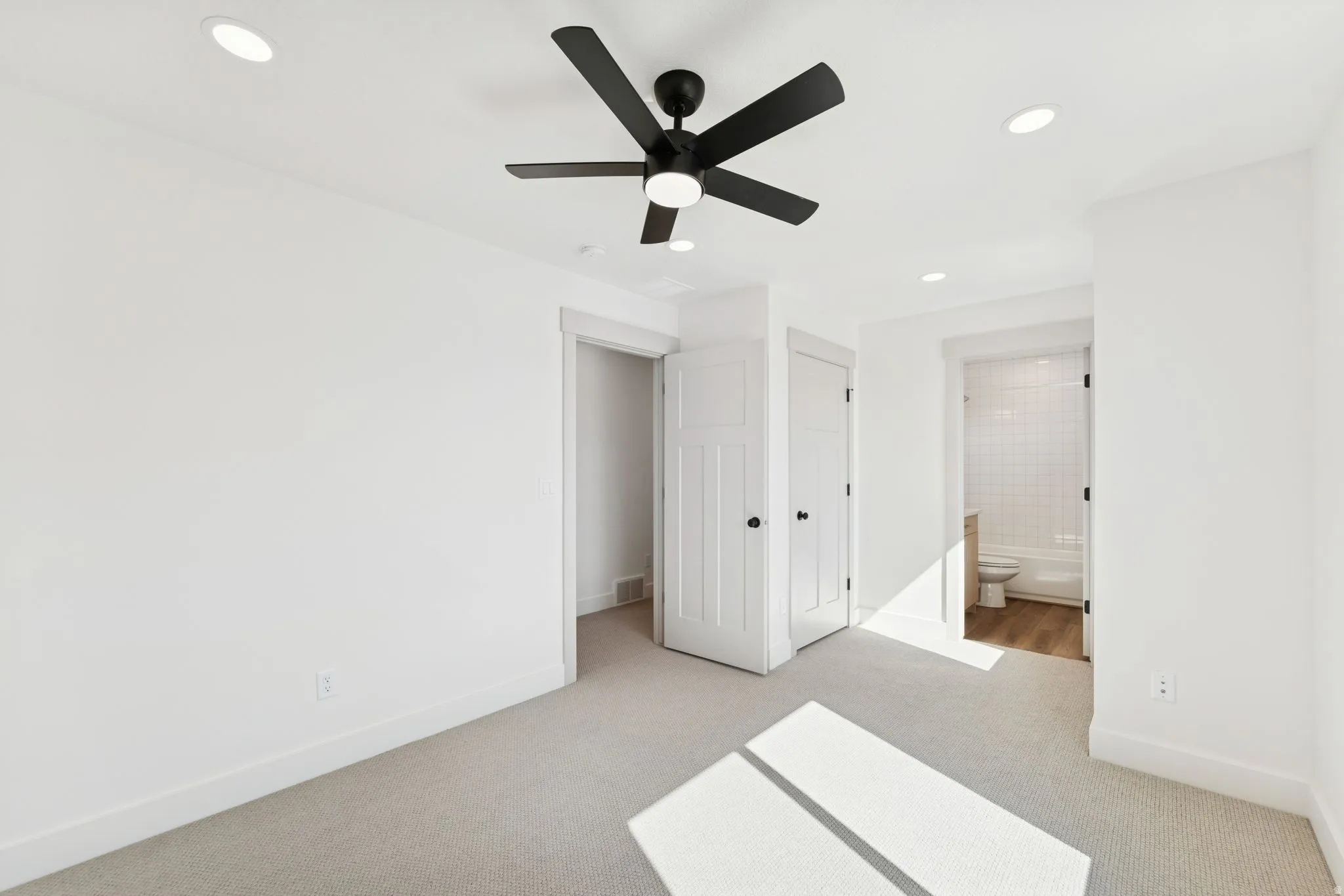 Unfurnished bedroom featuring light colored carpet, a closet, a ceiling fan, recessed lighting, and ensuite bathroom
