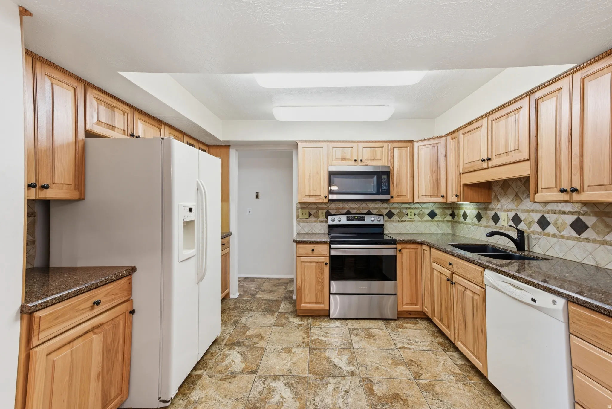 Kitchen with stainless steel appliances, dark stone countertops, light wood finish cabinets, and decorative backsplash