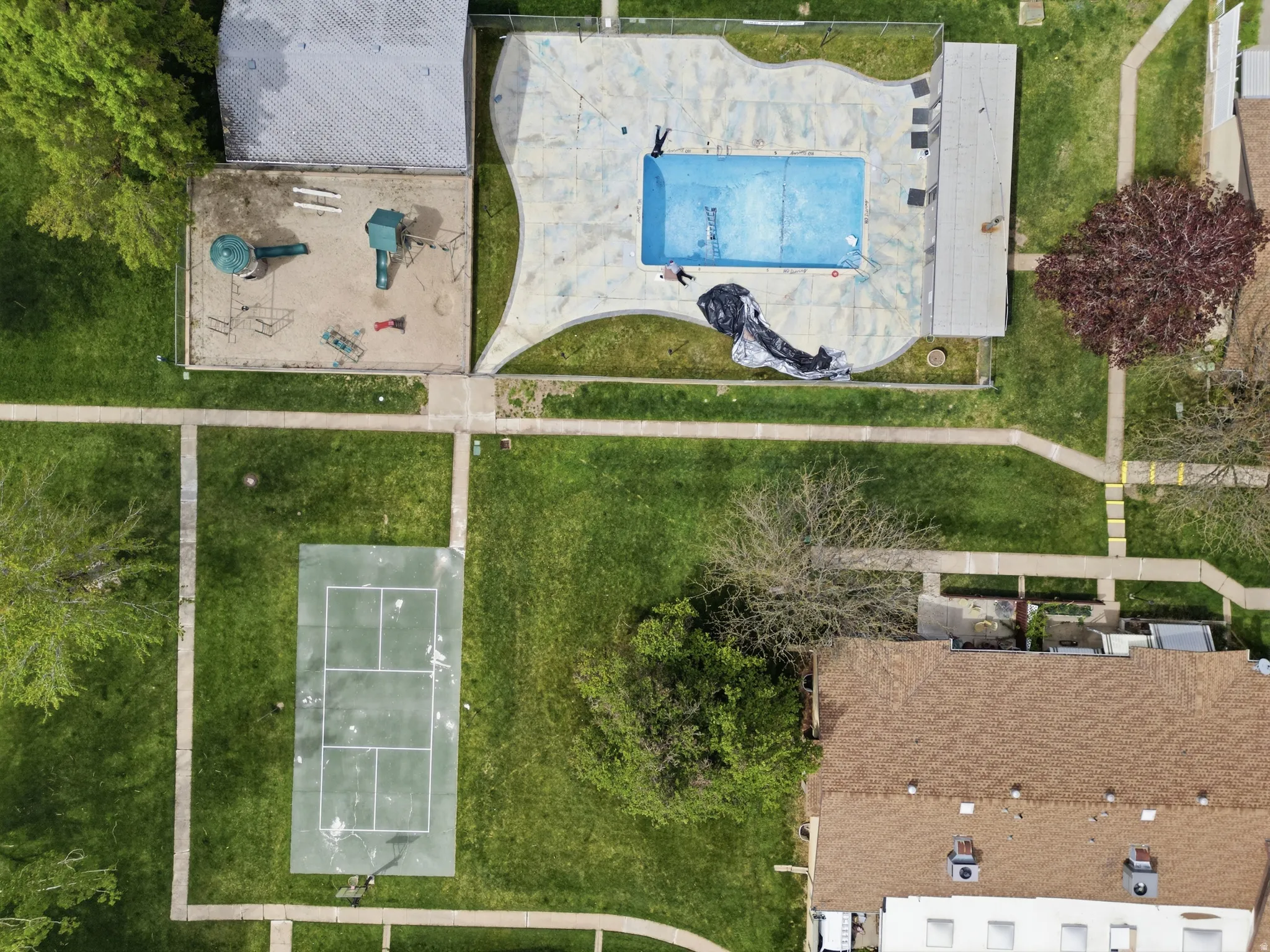 Aerial view of a pool, playground, tennis, courtyard.