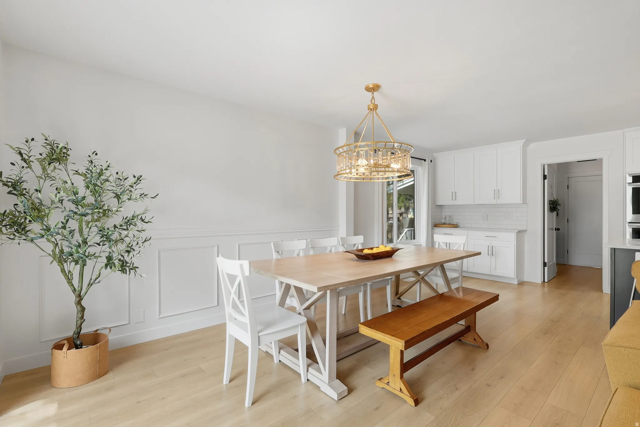 Dining space featuring light wood-type flooring, a decorative wall, a wainscoted wall, and hanging lights