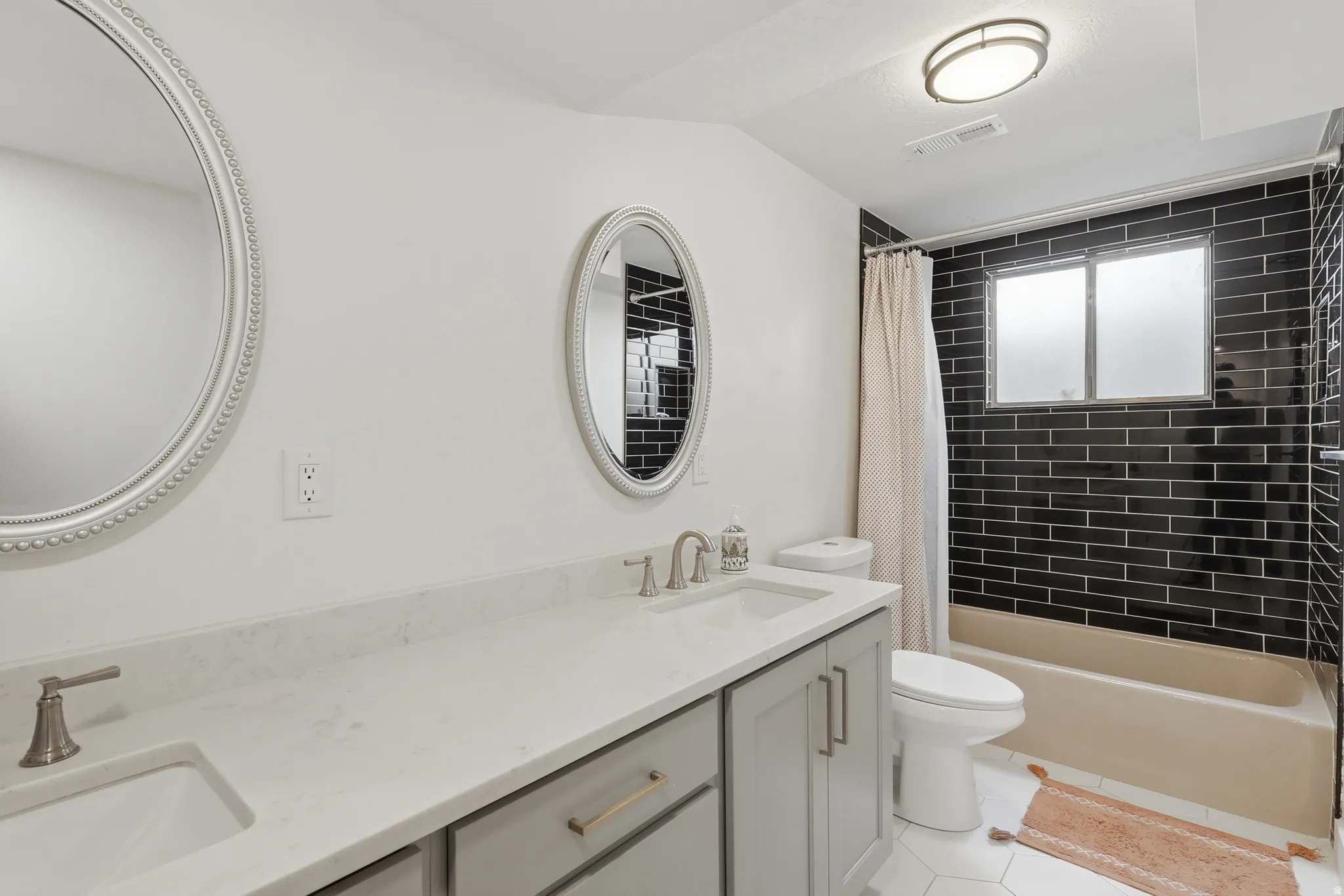 Bathroom featuring double vanity, shower / tub combo, and light tile patterned floors