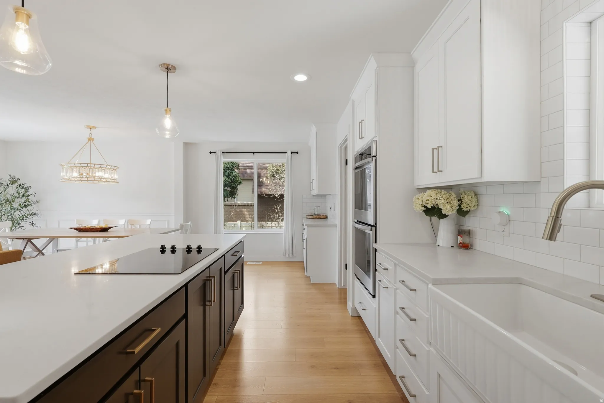 Kitchen featuring two tone cabinets, light wood-type flooring, black electric cooktop, backsplash, and light stone countertops
