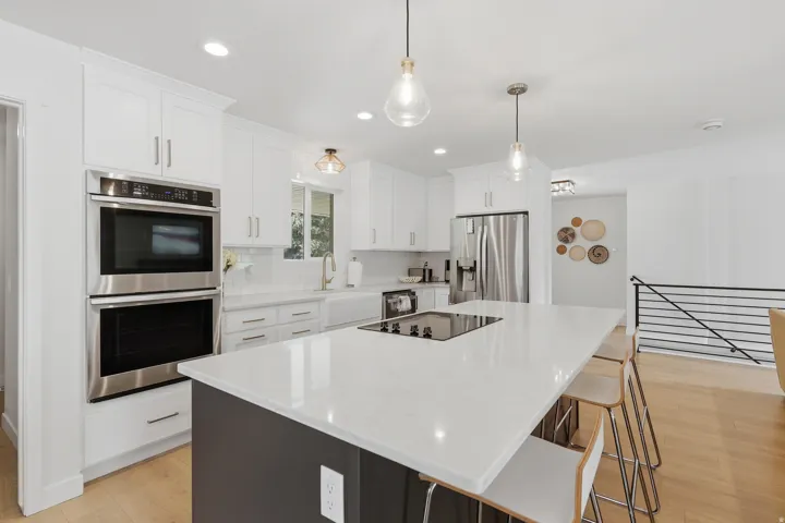 Dual tone kitchen with stainless steel appliances, light wood-style flooring, a center island, a breakfast bar, and light stone counters