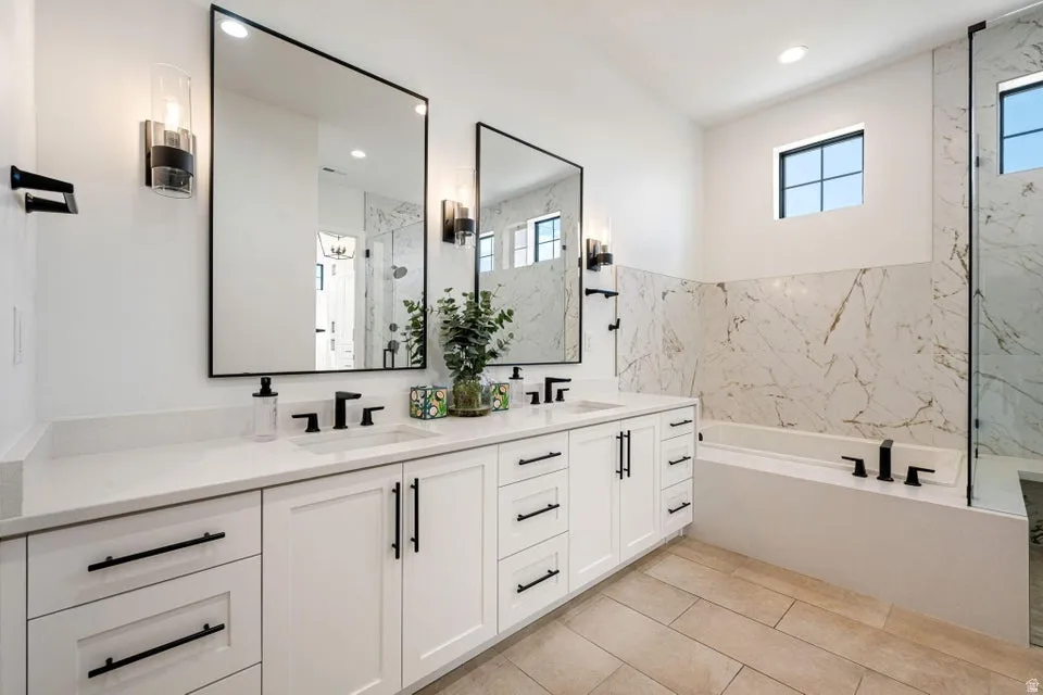 Full bath featuring healthy amount of natural light, double vanity, a garden tub, a marble finish shower, and recessed lighting