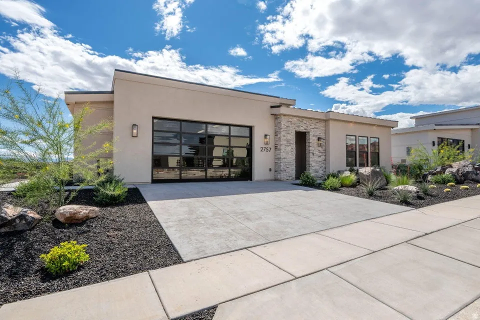 Modern home featuring an attached garage, concrete driveway, stucco siding, and stone siding