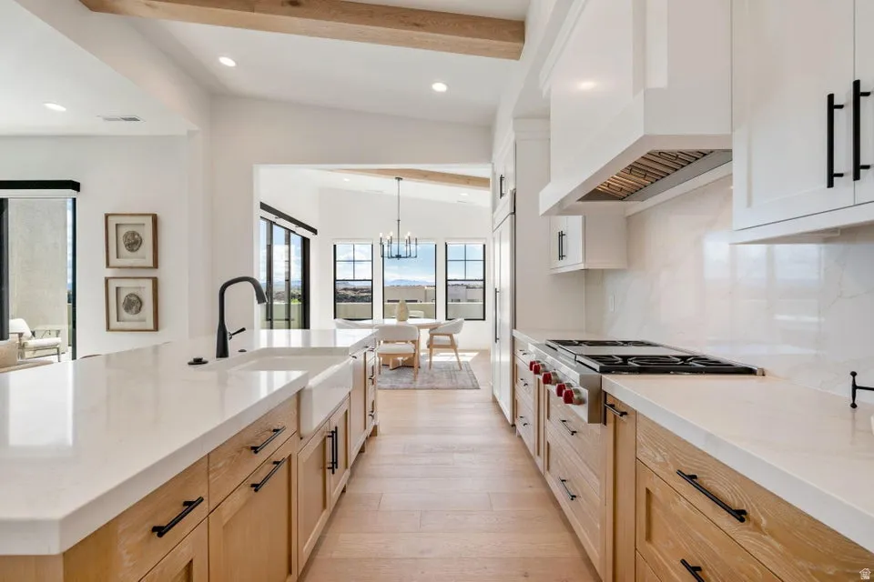 Two tone kitchen with a chandelier, stainless steel gas cooktop, light stone countertops, light wood-style flooring, and a large island
