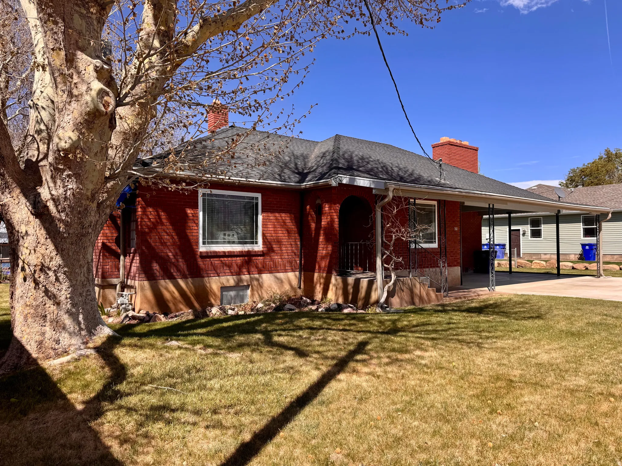 Back of house featuring a chimney, a lawn, brick siding, and a carport
