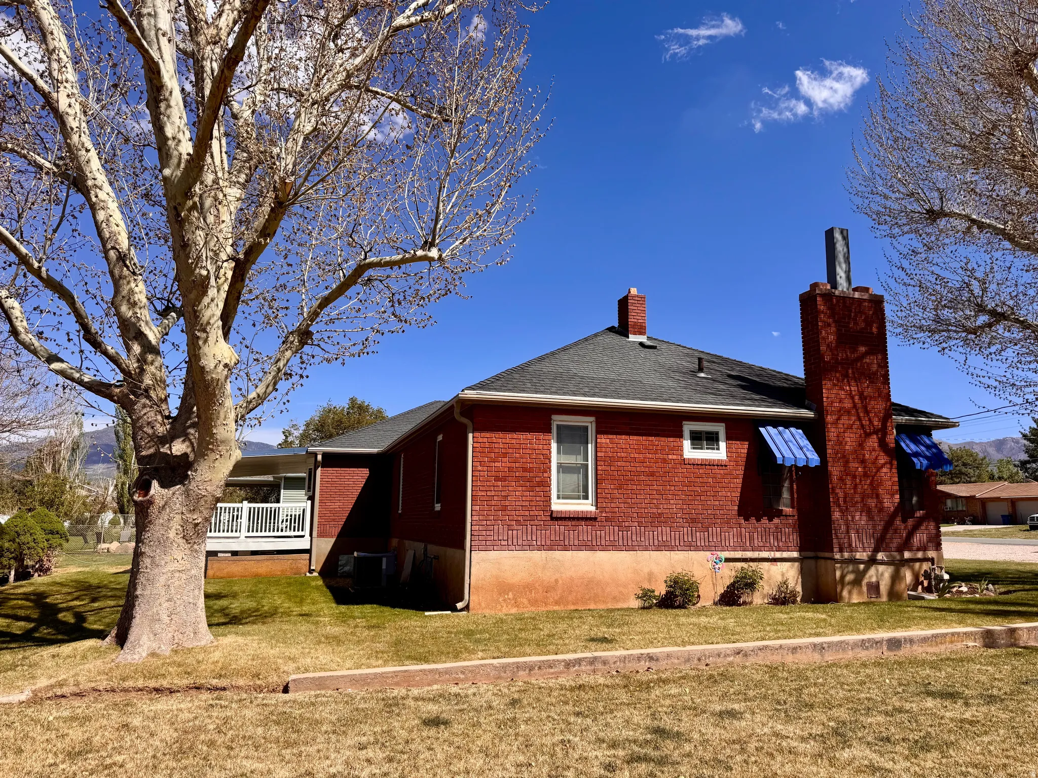 View of property exterior featuring a chimney, brick siding, a lawn, a deck, and roof with shingles