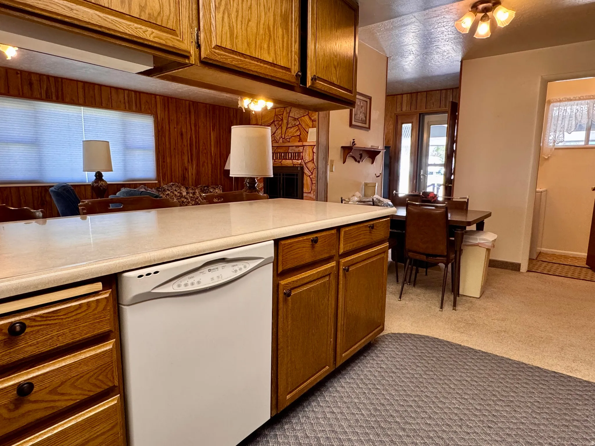 Kitchen with white dishwasher, light countertops, wood finish cabinetry, light carpet, and a textured ceiling