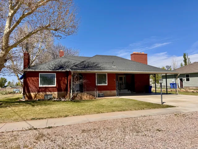 Single story home featuring a chimney, an attached carport, brick siding, driveway, and a front yard