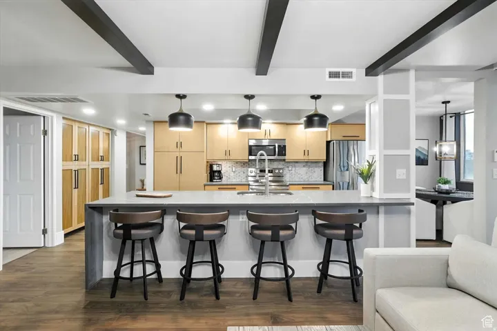 Kitchen with light cabinets, decorative backsplash, stainless steel appliances, and beamed ceiling