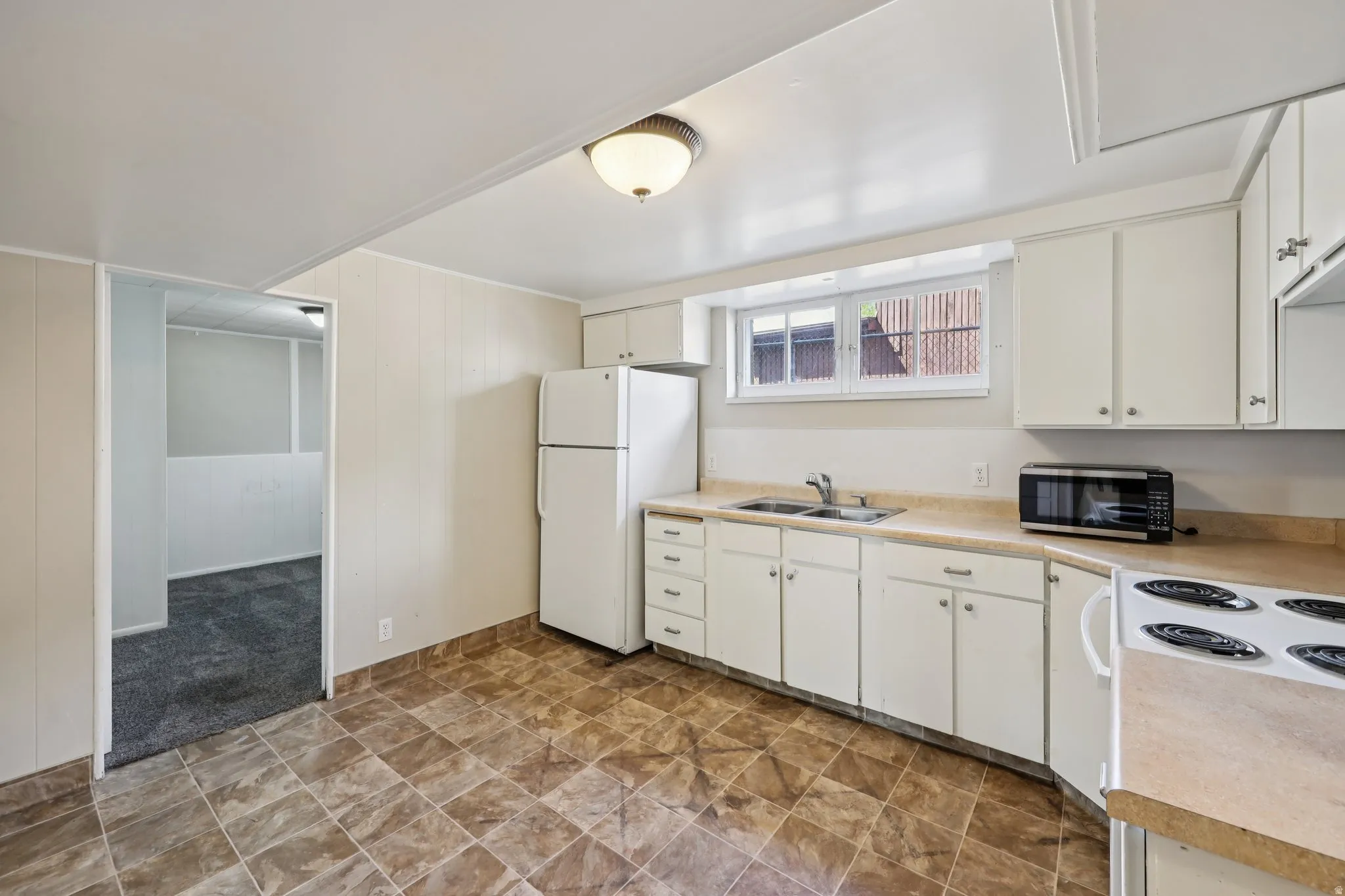 Kitchen featuring light countertops, white appliances, white cabinetry, light carpet, and wooden walls