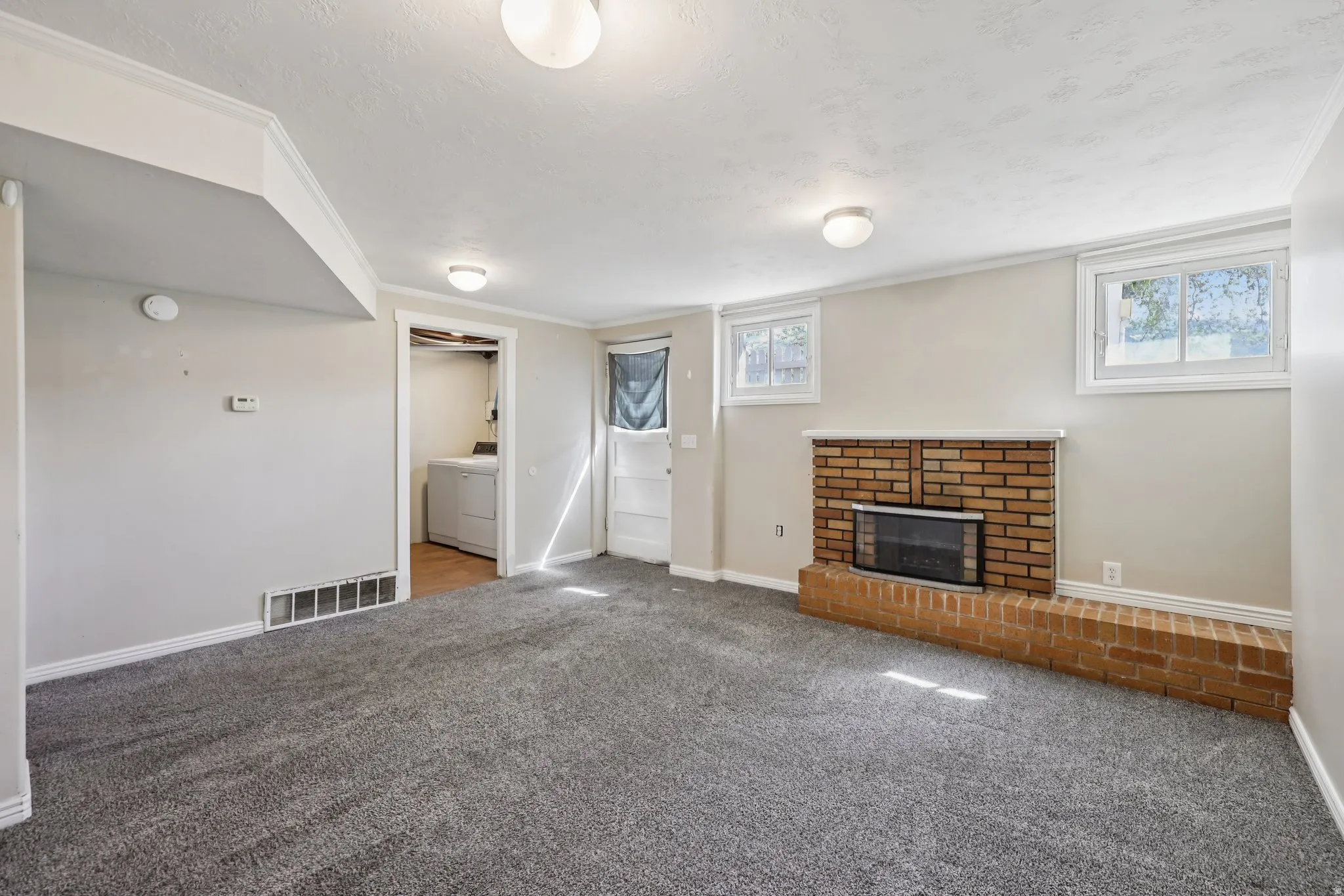 Unfurnished living room with carpet, a brick fireplace, crown molding, a textured ceiling, and separate washer and dryer