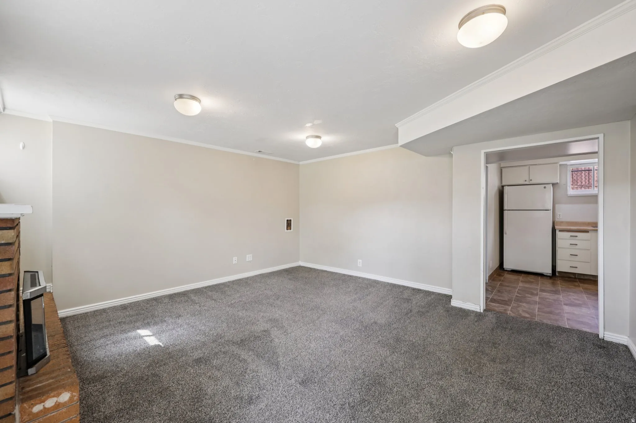 Unfurnished bedroom with freestanding refrigerator, ornamental molding, dark colored carpet, a closet, and a fireplace