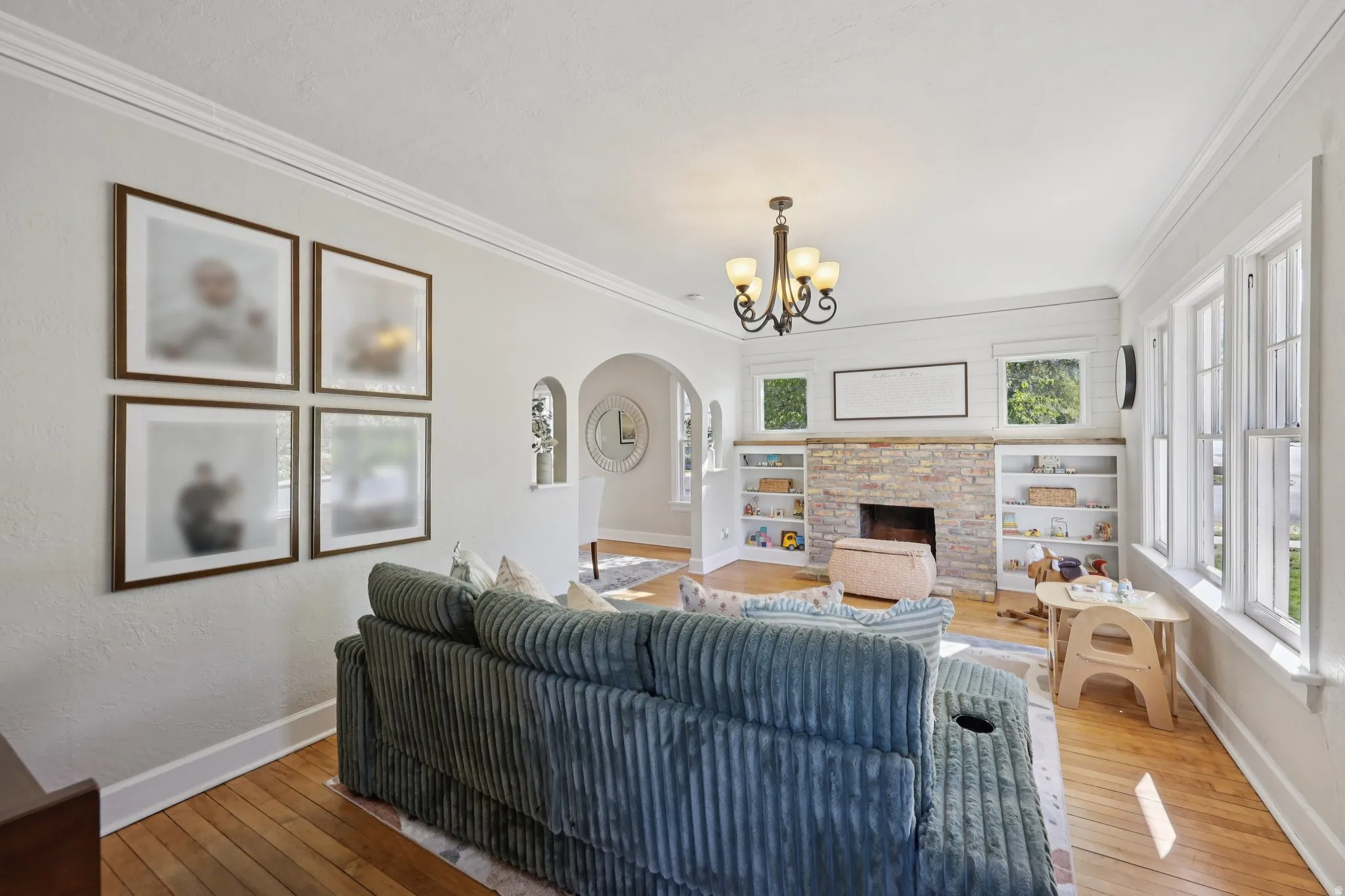 Living room featuring hardwood / wood-style floors, arched walkways, suspended lighting, ornamental molding, and a stone fireplace
