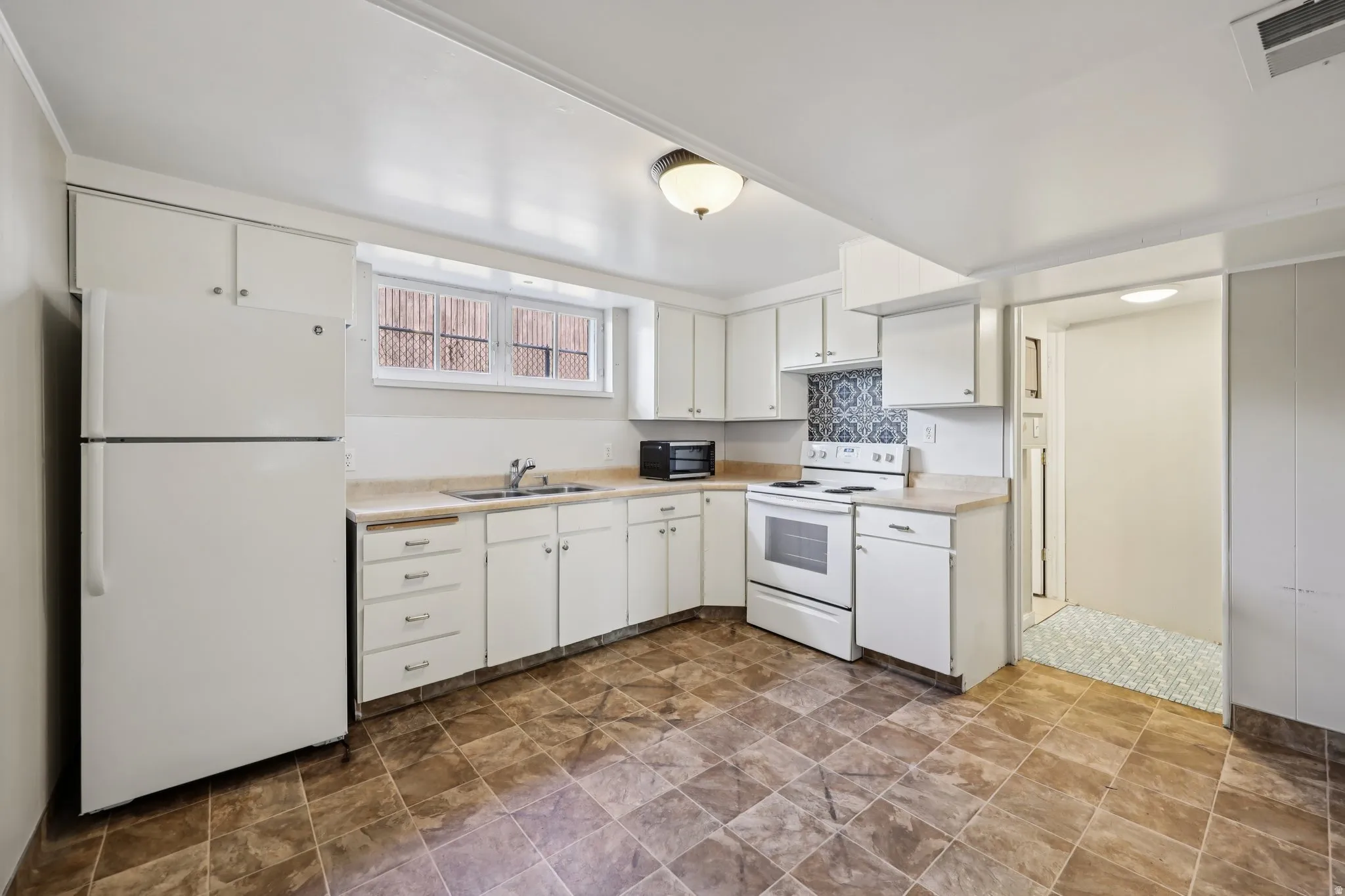 Kitchen with white appliances, stone finish floors, light countertops, and white cabinetry