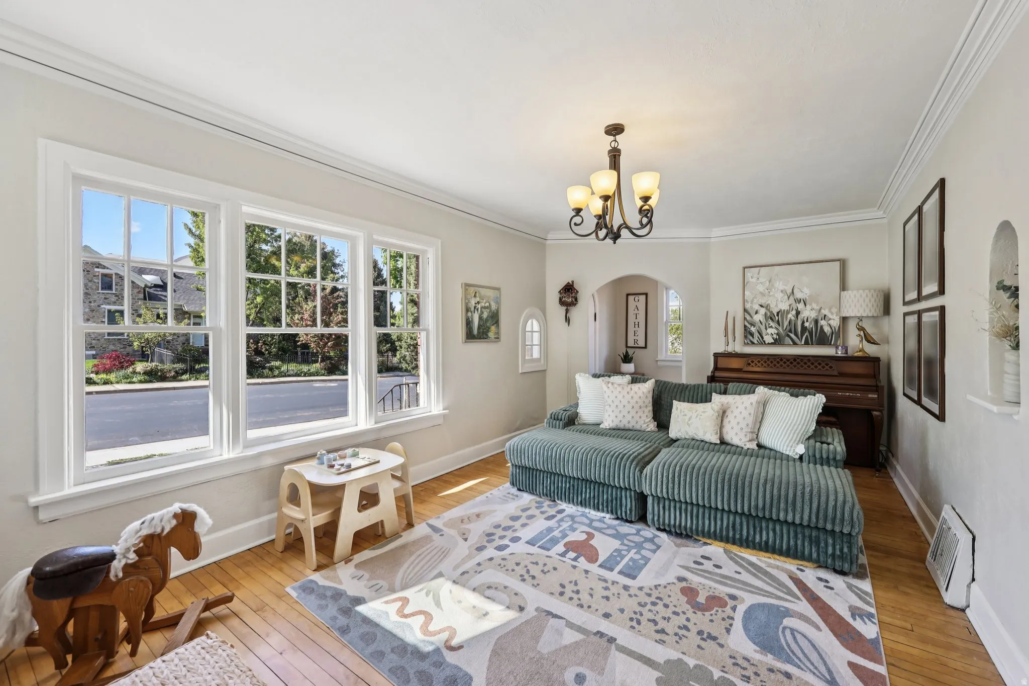 Living room with light wood finished floors, arched walkways, hanging lights, and crown molding