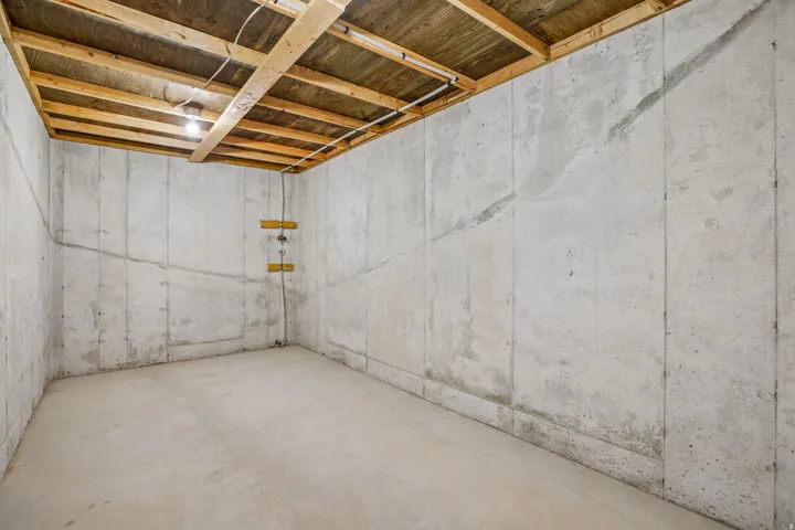 Unfinished basement with concrete walls and flooring, featuring exposed ceiling joists and integrated lighting