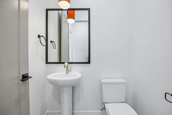 Pedestal sink with brushed nickel faucet, black framed mirror, and modern pendant lighting