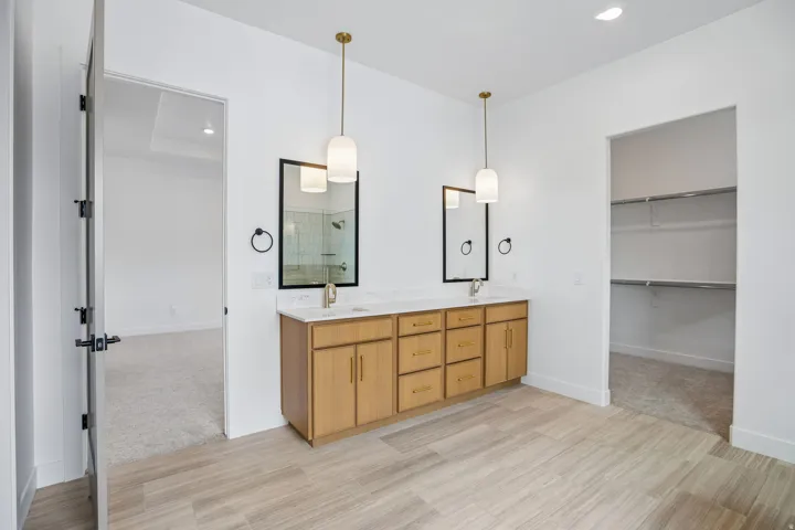 Dual wood-finish vanities with rectangular undermount sinks, quartz countertops, and gold-tone fixtures