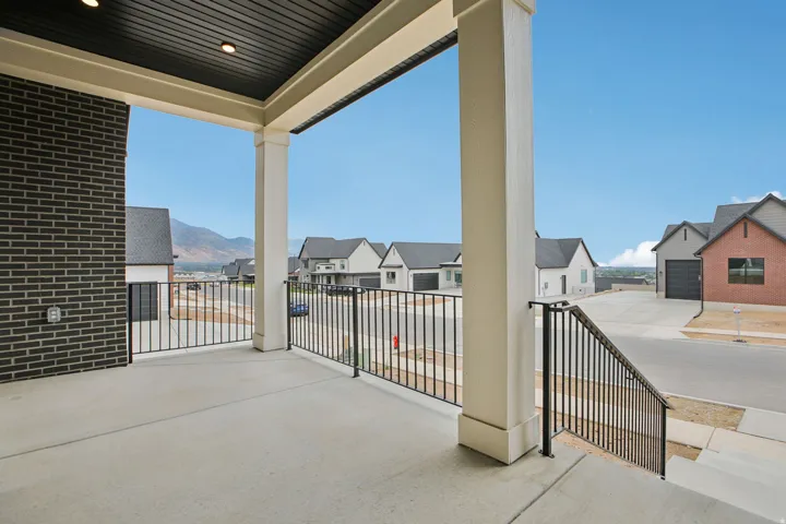 Concrete covered porch with black metal railing and dark brick exterior