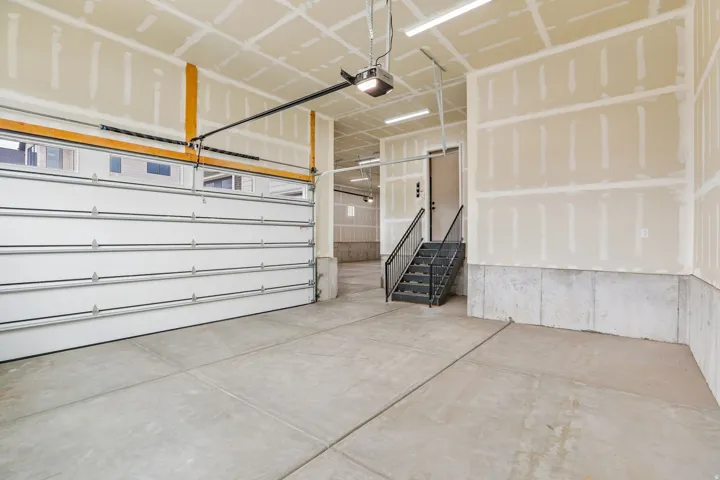 Spacious garage featuring a concrete floor, overhead lighting, an automatic garage door opener, and interior stairs with a black metal railing