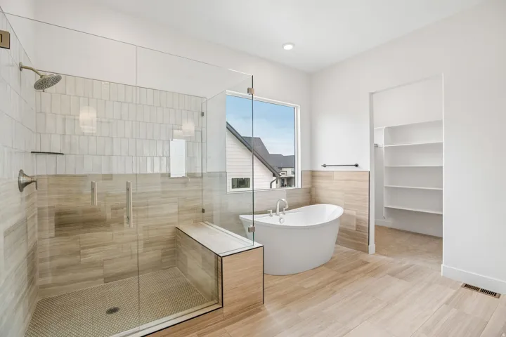 Glass-enclosed shower with a built-in bench, freestanding soaking tub, wood-finish flooring, and built-in shelving