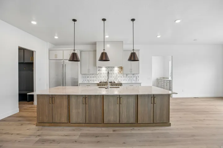 Spacious kitchen island with integrated storage, light-toned wood-finish flooring, recessed ceiling lights, and three pendant light fixtures