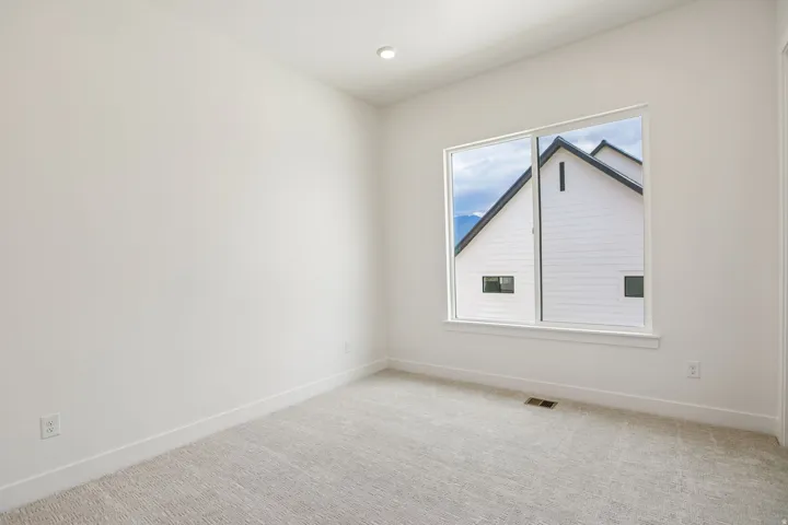 Recessed ceiling lighting, white painted walls, large window, and light-colored carpeting