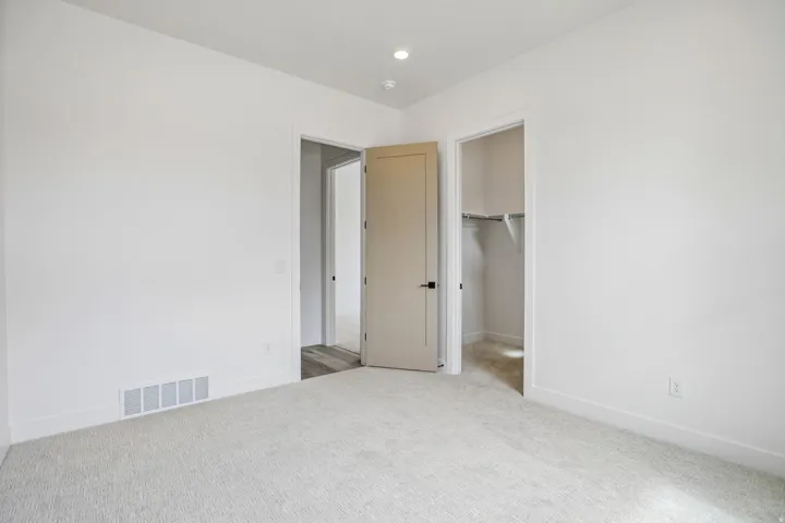 Neutral carpeting, recessed lighting, white walls, and a flat-panel door with matte black hardware