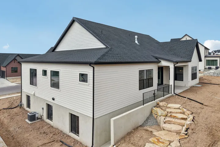 Modern exterior with light siding, dark-framed windows, and a covered patio featuring a black metal railing