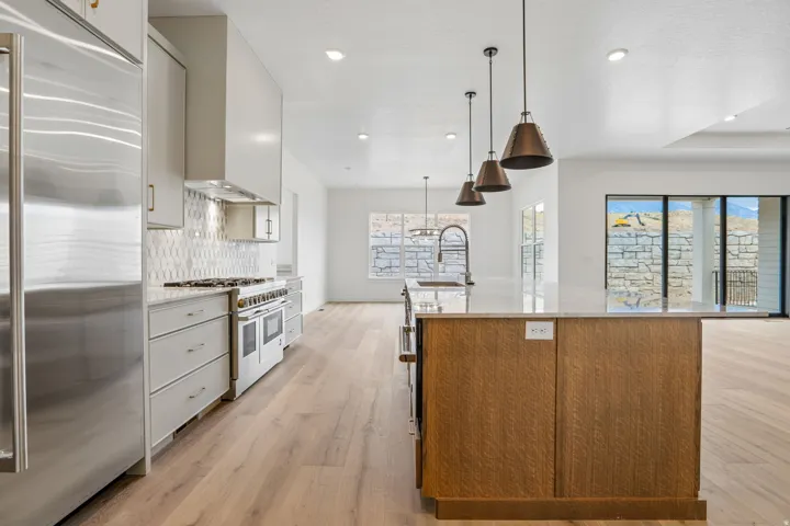 Kitchen featuring stainless steel appliances, light wood-finish flooring, a large island with a built-in sink, and pendant lighting