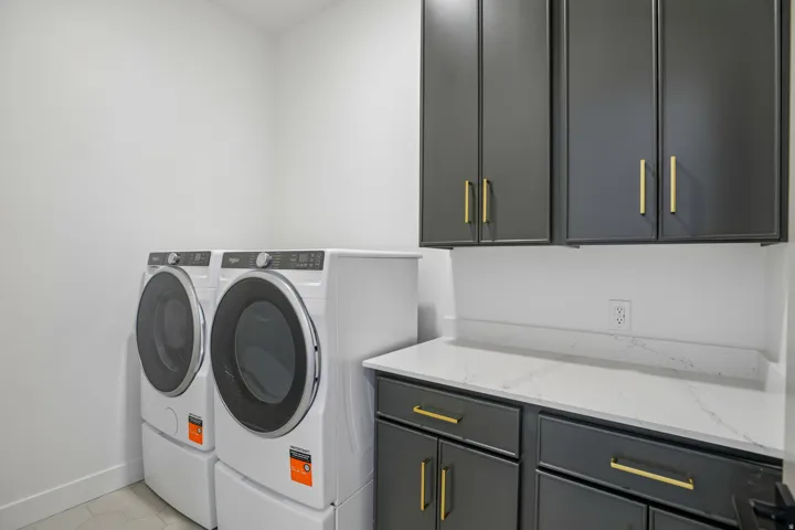 Laundry area featuring dark cabinetry with gold-tone hardware, a white countertop, and white walls
