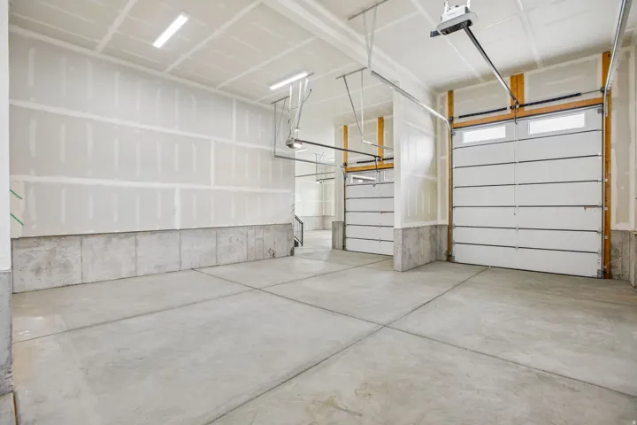 Spacious garage with concrete flooring, two overhead garage doors with integrated windows, and exposed ceiling joists