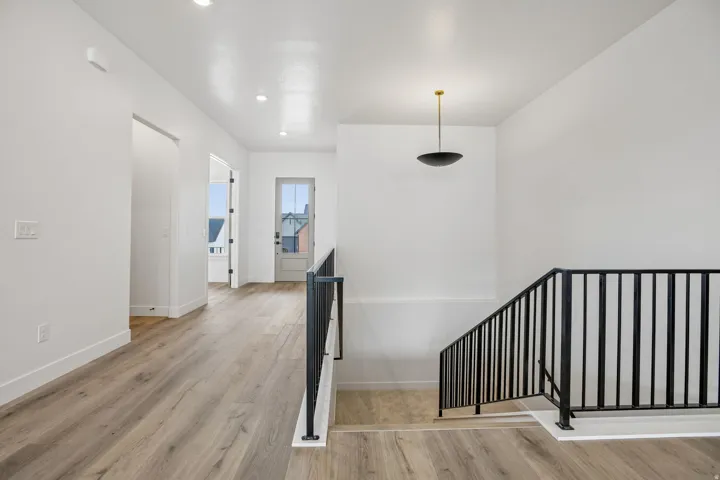Wood-finish flooring throughout, modern black metal railing, recessed ceiling lighting, and a contemporary pendant light fixture