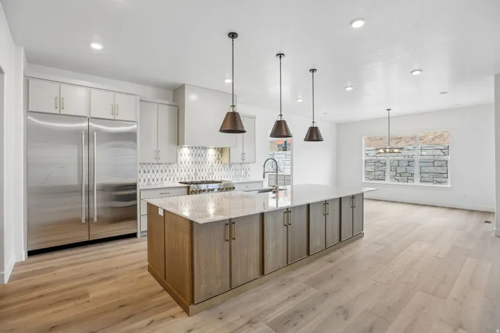 Kitchen featuring stainless steel appliances, a large island with an integrated sink, pendant lighting, and wood-finish flooring