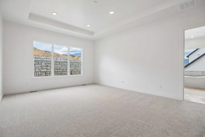 Bright room featuring a large window, recessed ceiling lighting, light-toned carpet flooring, and a tray ceiling